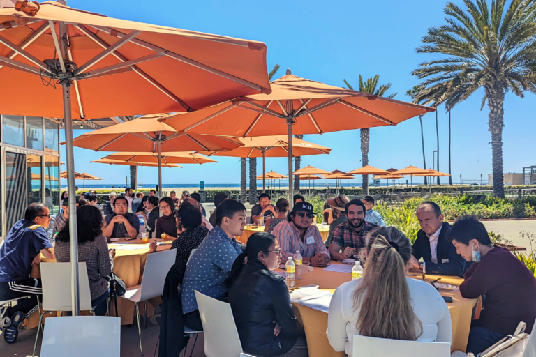 Attendees (faculty, postdoctoral scholars, graduate students, and staff) seated at tables outdoors, participating in a lunch discussion on Responsible Conduct of Research at the Neurobehavioral Genetics Retreat hosted on May 12, 2022 at the Annenberg Community Beach House.