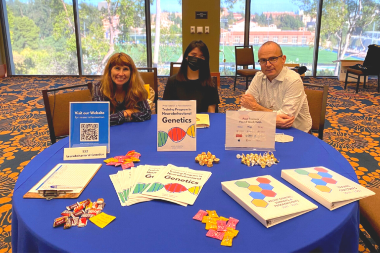 Drs. Carrie Bearden and Roel Ophoff seated at a table for the Training Program in Neurobehavioral Genetics set up at the NSIDP Retreat Resource Fair on September 29, 2022.